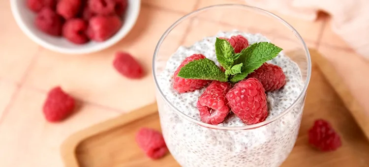 Przepis na lody kokosowe z chia – prosty deser bez użycia blendera Zdrowy pudding z nasionami chia, udekorowany świeżą miętą i czerwonymi owocami, podany na drewnianej tacy na jasnoróżowym tle