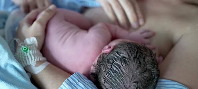 Malutkie niemowlę jest karmione piersią bezpośrednio na ciele mamy na tle jasnoniebieskiego materiału