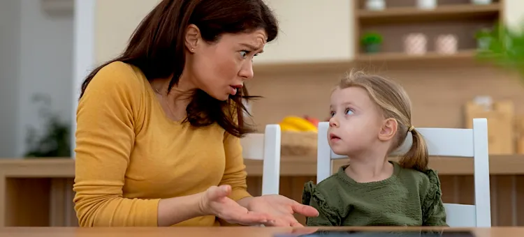 Dlaczego dziecko kłamie? Najczęstsze powody Zaskoczona mama w żółtej bluzce rozmawia z małą córeczką przy drewnianym stole kuchennym