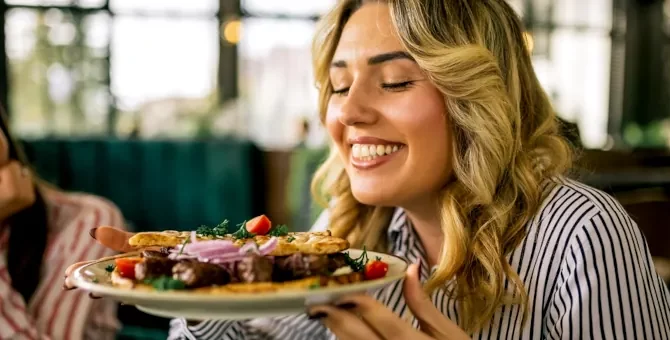 Uśmiechnięta blondynka delektuje się aromatem grillowanego mięsa z warzywami podanego na jasnym talerzu w restauracji