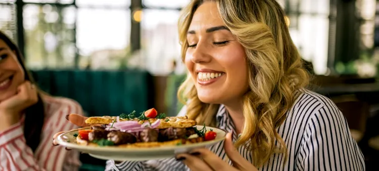 Uśmiechnięta blondynka delektuje się aromatem grillowanego mięsa z warzywami podanego na jasnym talerzu w restauracji