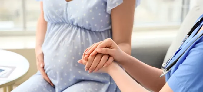 Wsparcie medyczne udzielane przyszłej mamie podczas wizyty w gabinecie lekarskim, zbliżenie na ręce lekarki, trzymające ręce pacjentki
