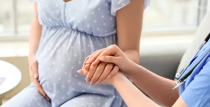 Wsparcie medyczne udzielane przyszłej mamie podczas wizyty w gabinecie lekarskim, zbliżenie na ręce lekarki, trzymające ręce pacjentki