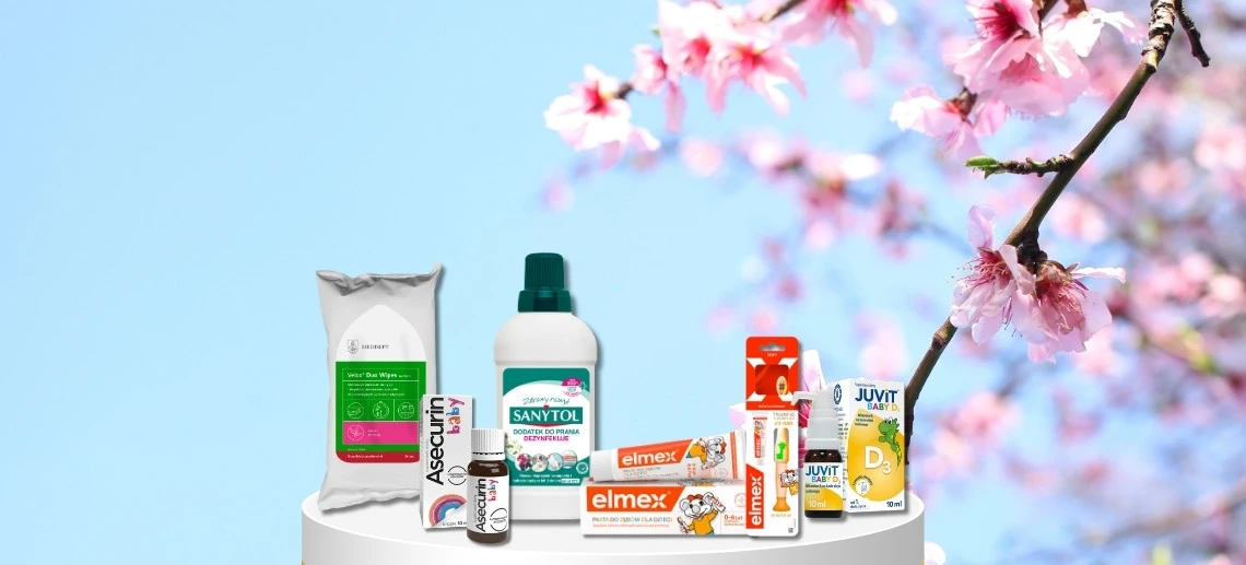 Produkty Sanytol, Asecurin baby, elmex®, Velox Duo Wipes i Juvit Baby D3 na tle kwitnących różowych gałęzi