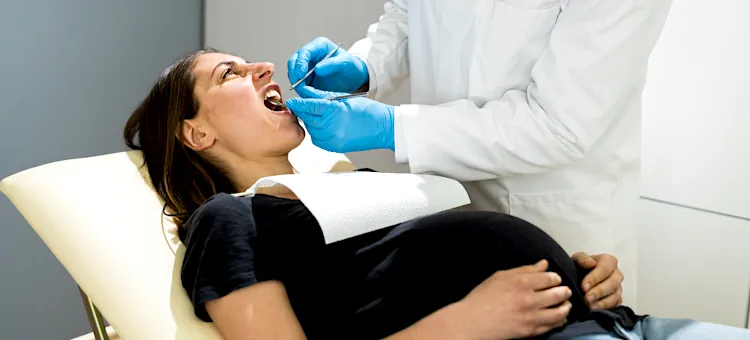 Leczenie zębów w ciąży – co jest bezpieczne, a czego unikać? Kobieta w ciąży podczas rutynowej kontroli uzębienia na jasnym fotelu dentystycznym
