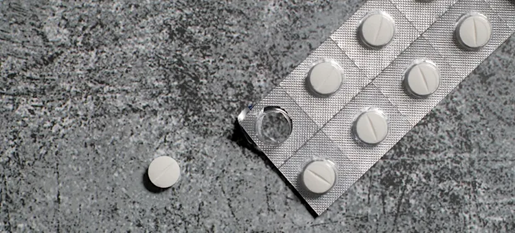Przyczyny zespołu Reye'a – jaki ma związek z aspiryną? Białe farmaceutyki ułożone na szarym kamiennym podłożu