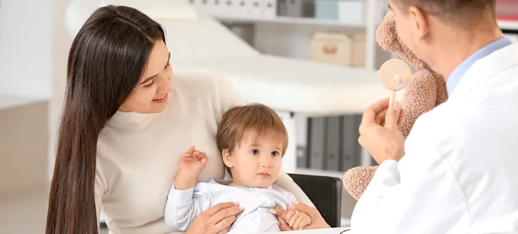 Laktoferyna od jakiego wieku? W jasnym wnętrzu gabinetu lekarskiego specjalista używa pluszowej zabawki podczas kontrolnej wizyty małego dziecka z mamą