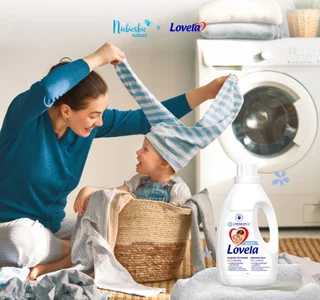 Mama z dzieckiem przy pralce oraz płyn do prania Lovela Baby – Niebieskie Pudełko