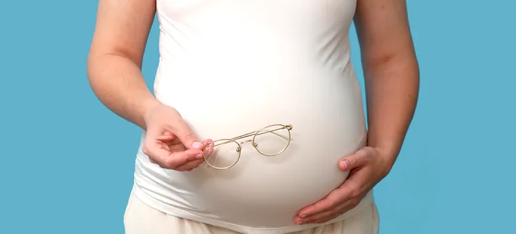 Wzrok w ciąży i po porodzie – czy może się pogorszyć? Przyszła mama z delikatnymi oprawkami korekcyjnymi na tle w kolorze jasnoniebieskim, zbliżenie na brzuch