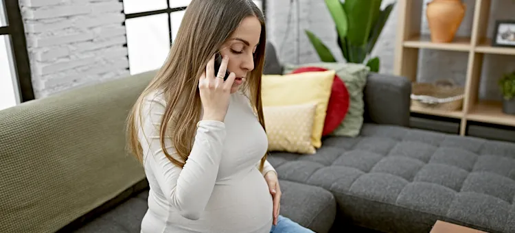 Kontakt z odrą w ciąży – co powinna zrobić ciężarna? Przyszła mama siedząca na ciemnoszarej kanapie z kolorowymi poduszkami prowadzi rozmowę telefoniczną