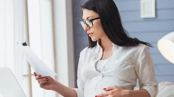 Ciężarna w okularach analizuje ważne pisma w jasnym biurowym wnętrzu