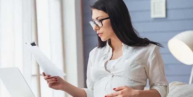 Ciężarna w okularach analizuje ważne pisma w jasnym biurowym wnętrzu