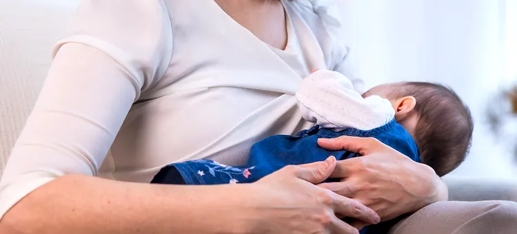 Przerwa na karmienie – do kiedy można z niej korzystać? Kobieta w białej bluzce przytula swoje dziecko na tle jasnego wnętrza