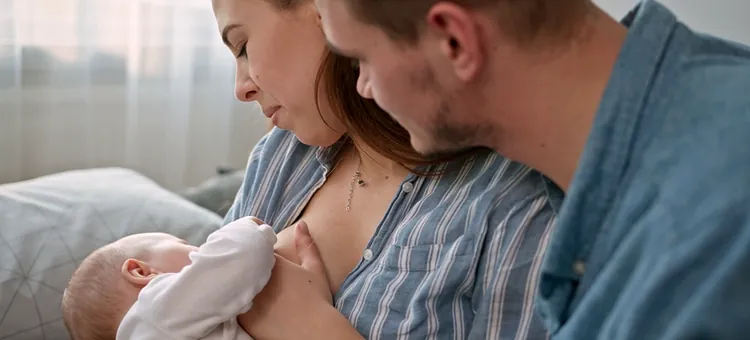 Czuły tata wspiera partnerkę podczas karmienia piersią noworodka w jasnej sypialni