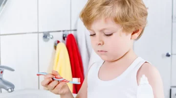 Dziecko trzymające akcesorium do higieny jamy ustnej na tle jasnych płytek łazienkowych