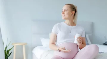 Uśmiechnięta ciężarna trzymająca suplementy diety w jasnej sypialni