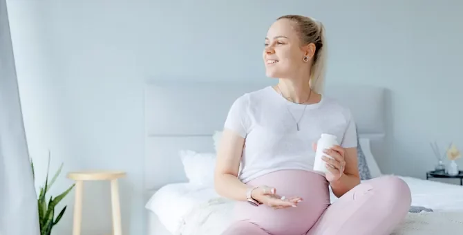 Uśmiechnięta ciężarna trzymająca suplementy diety w jasnej sypialni