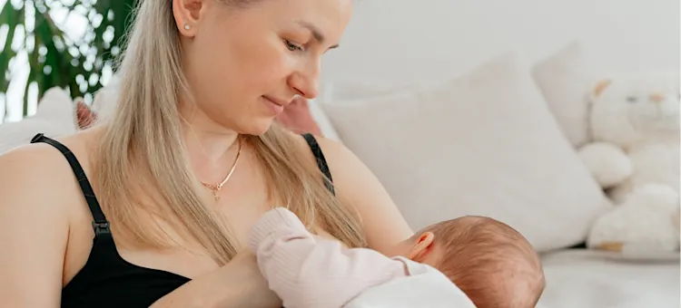 Czuła kobieta przytula swoje dziecko podczas karmienia piersią na tle jasnej kanapy z poduszkami
