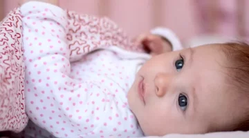 Uśmiechnięty maluch w jasnych śpioszkachodpoczywa na miękkim podłożu