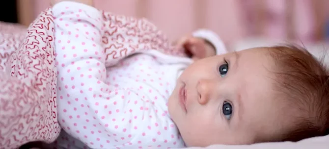 Uśmiechnięty maluch w jasnych śpioszkachodpoczywa na miękkim podłożu