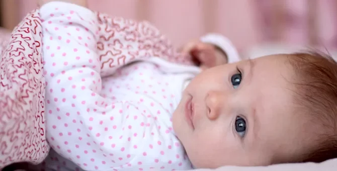 Uśmiechnięty maluch w jasnych śpioszkachodpoczywa na miękkim podłożu